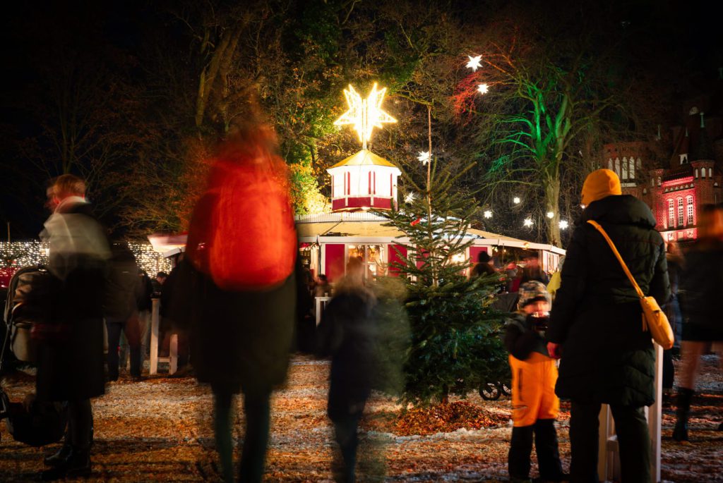 Ein Weihnachtsmarkt bei Nacht mit beleuchteten Sternen und Menschen im Vordergrund.