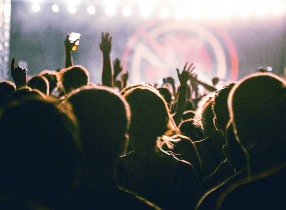 Menschenmenge vor einer Bühne, Hände in der Luft, im Hintergrund leuchtende Bühne