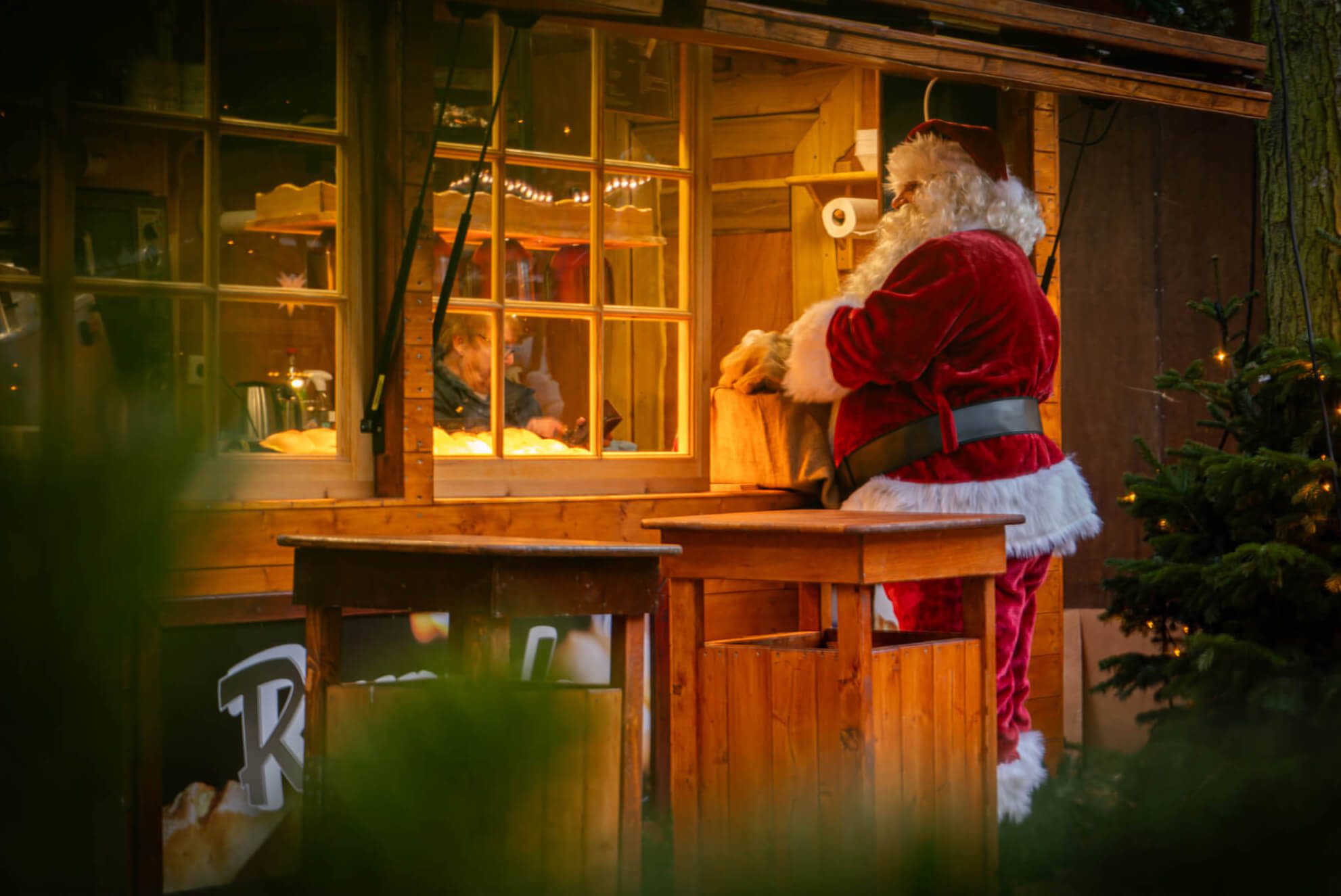 Ein Weihnachtsmann steht am Fenster eines Holzhäuschens.