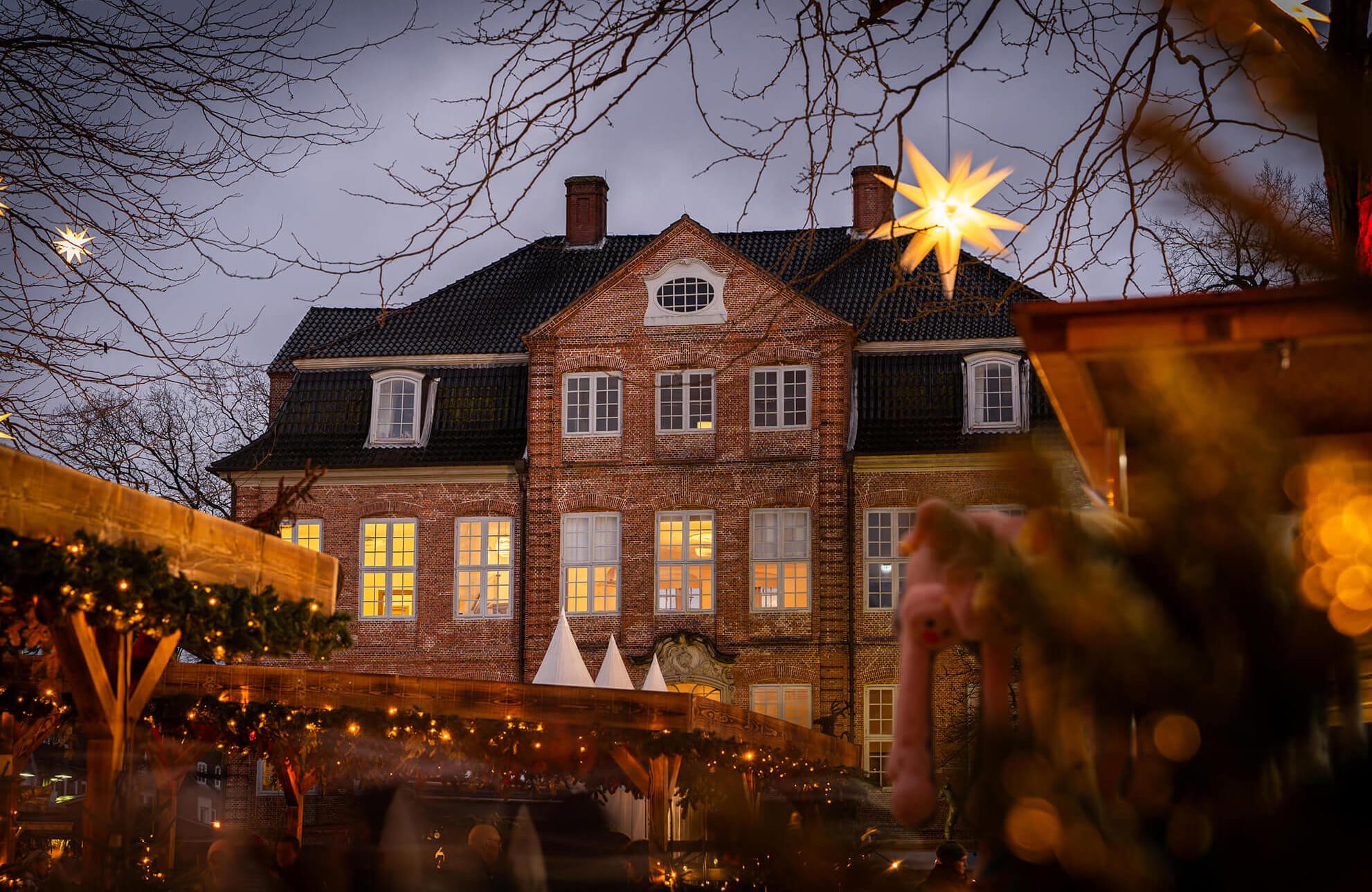 Ein beleuchtetes Backsteingebäude, eingerahmt von weihnachtlicher Dekoration.