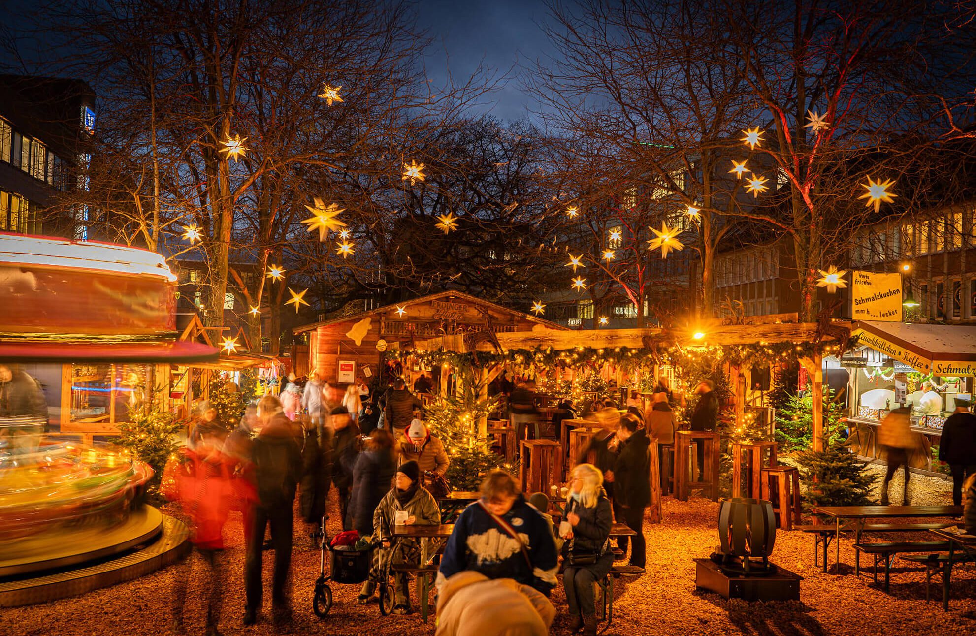 Weihnachtsmarkt bei Nacht mit Lichtersternen und Menschen.