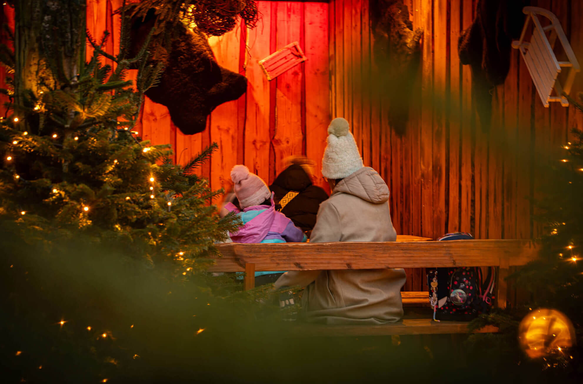 Menschen, darunter Kinder mit Mützen, sitzen auf einer Bank in einem weihnachtlich geschmückten Raum.