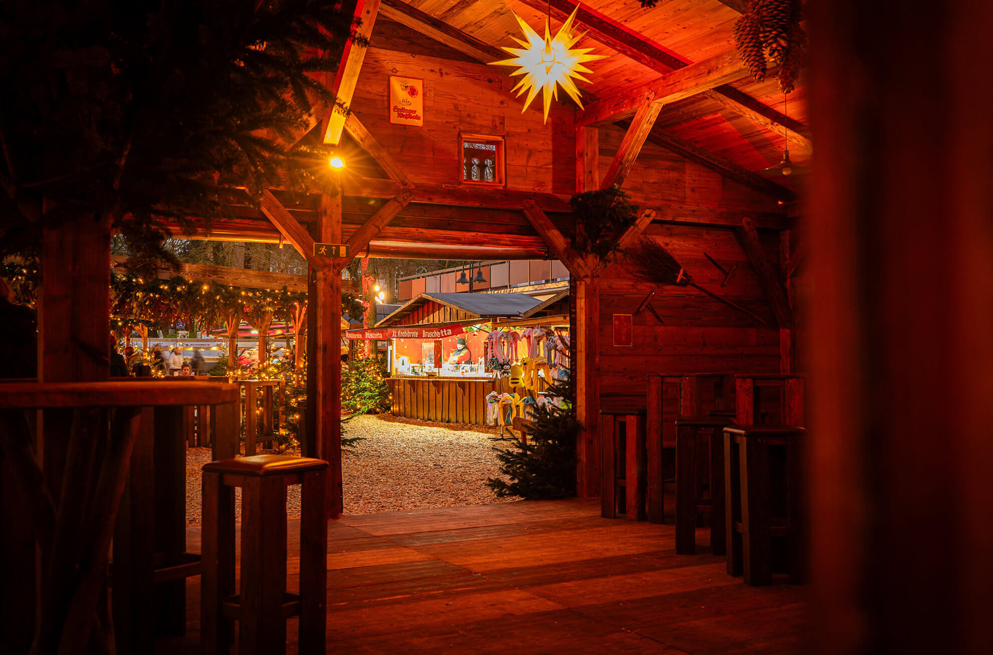 Blick aus einer Holzhütte auf einen geschmückten Weihnachtsmarktstand.