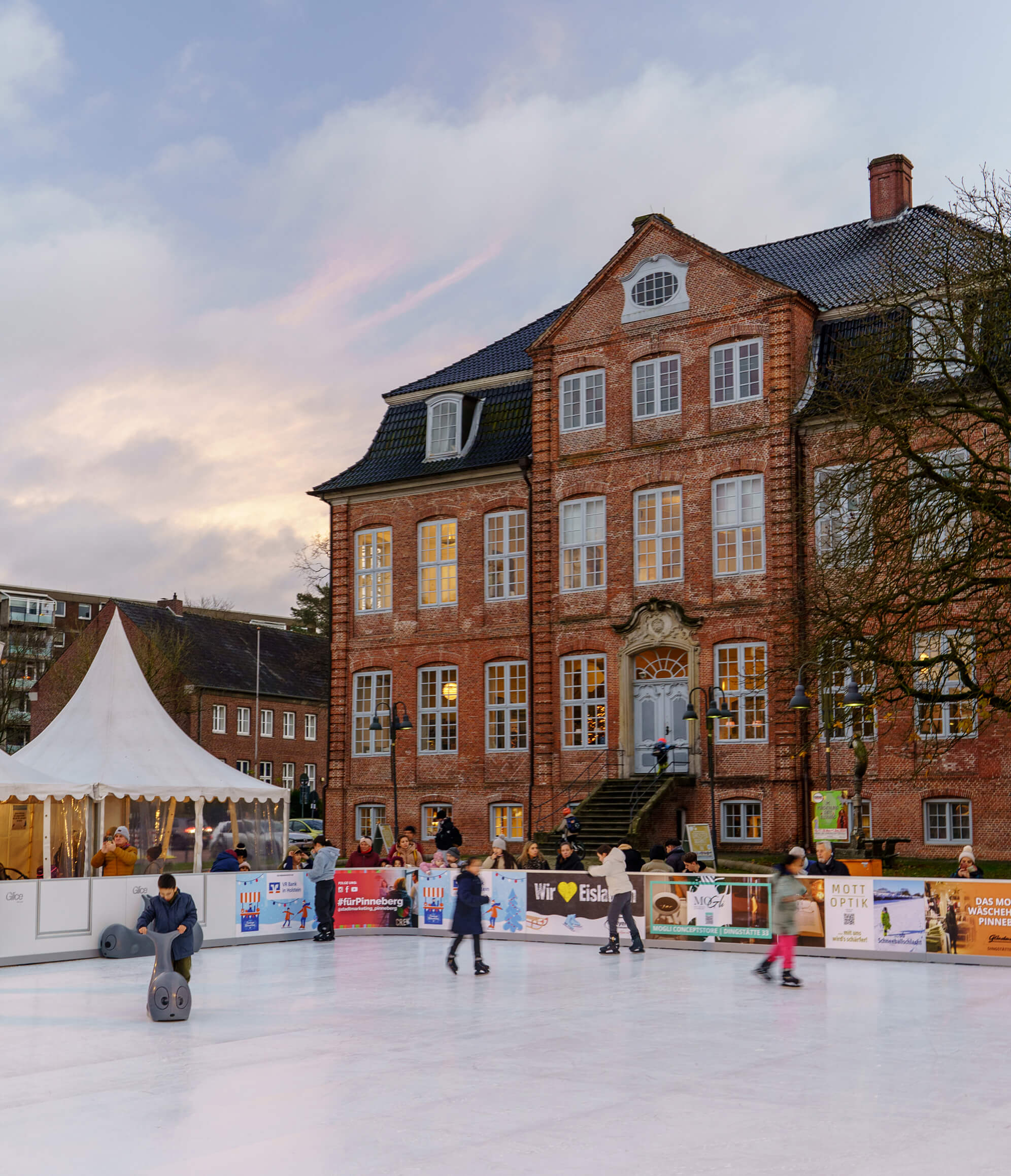 Eine Eislaufbahn vor einem historischen Gebäude, umgeben von Menschen.