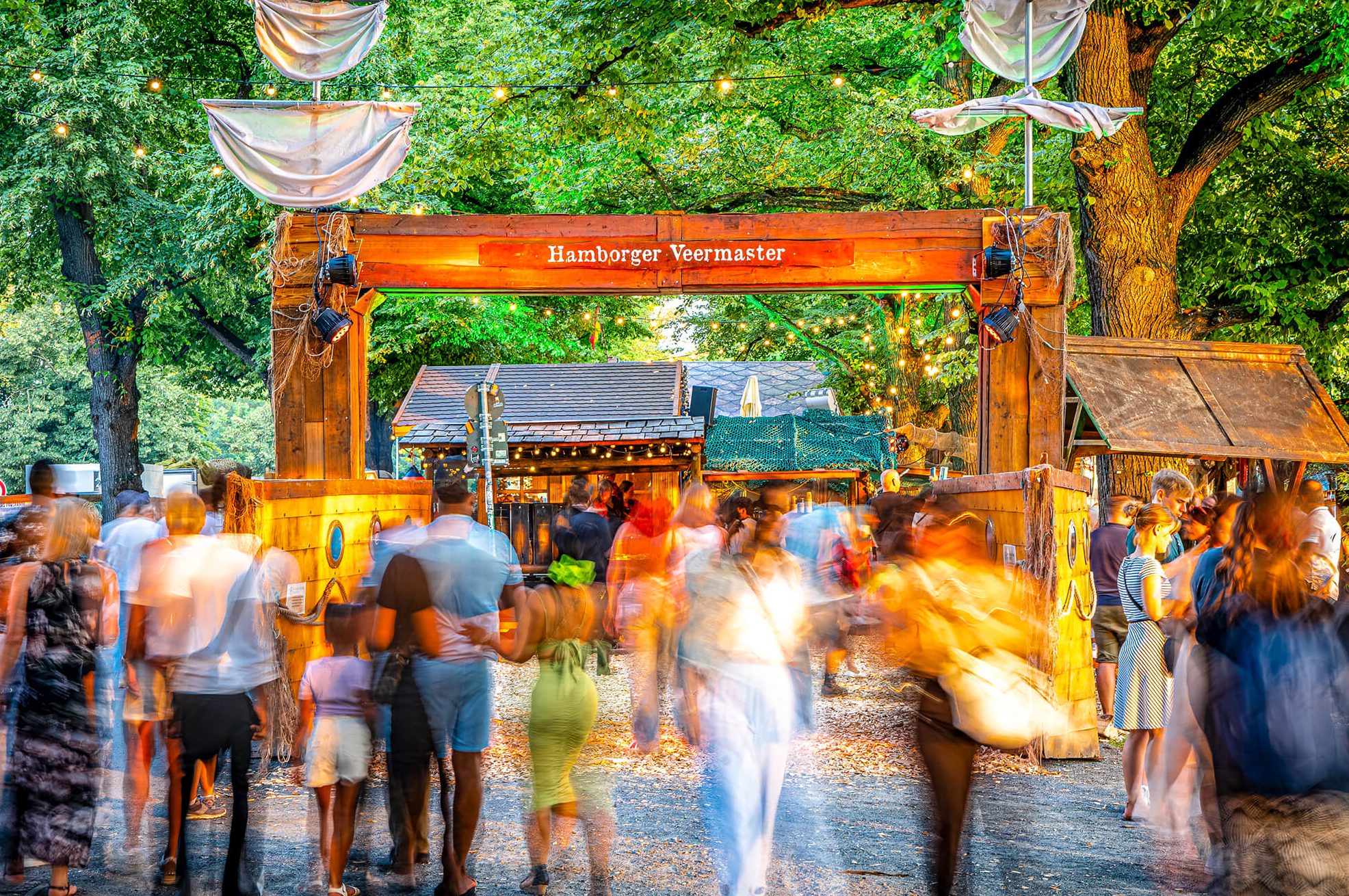 Menschenmenge unter einer Holzbogenkonstruktion mit dem Namen "Hamborger Veermaster"
