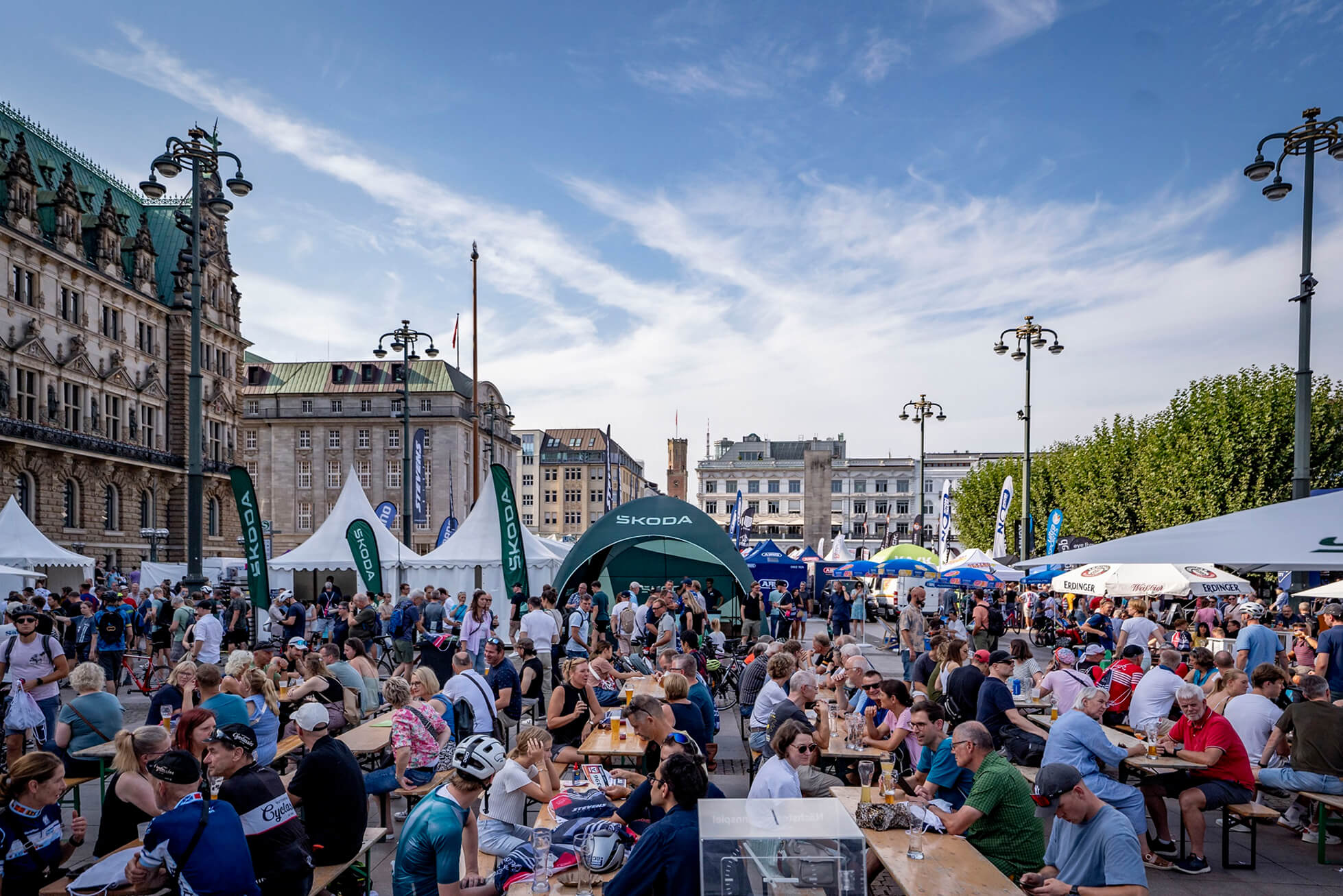 Menschen bei einem Outdoor-Event im Sonnenschein, umgeben von Ständen und Gebäuden.