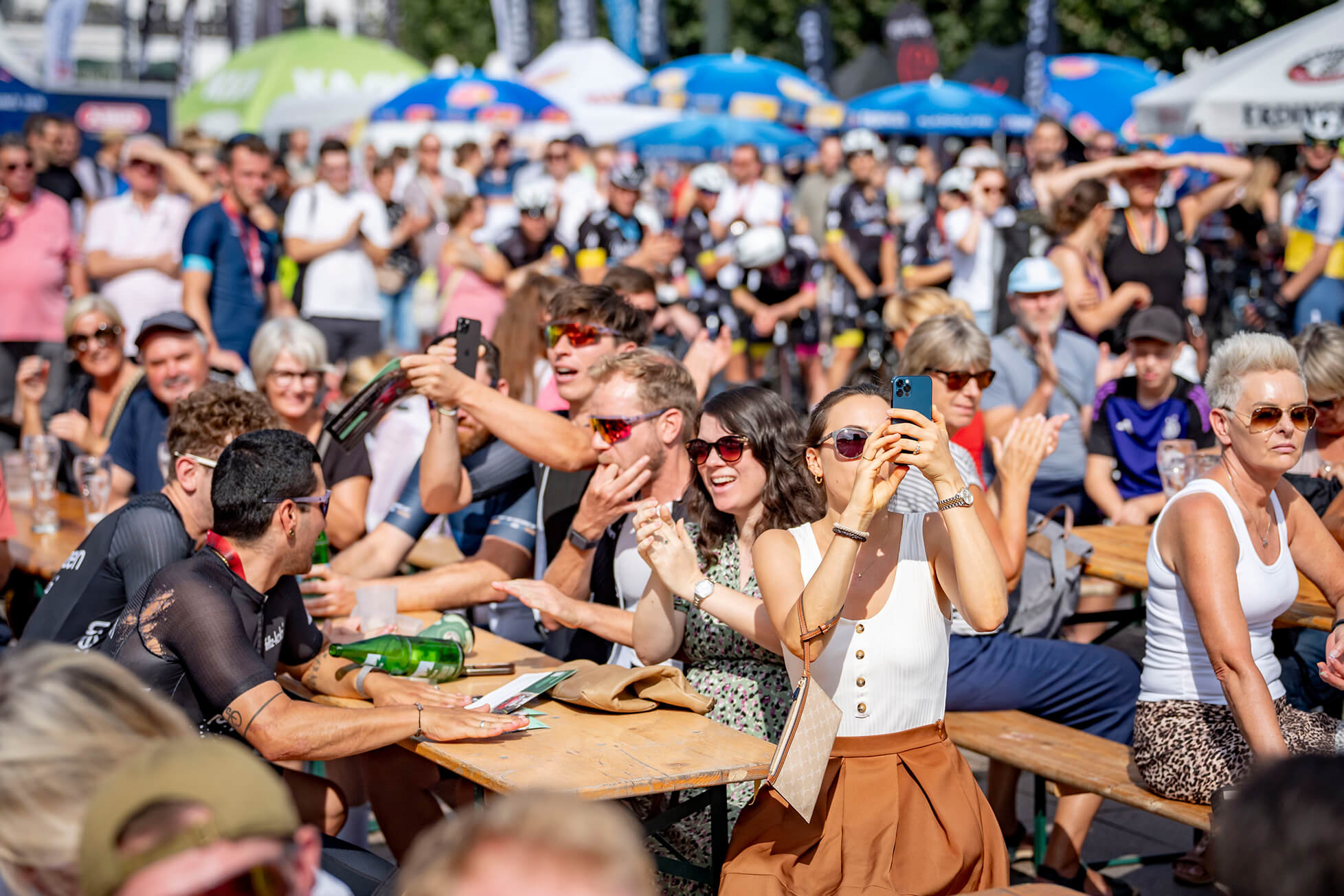 Eine Gruppe von Menschen sitzt an Biertischen und applaudiert.