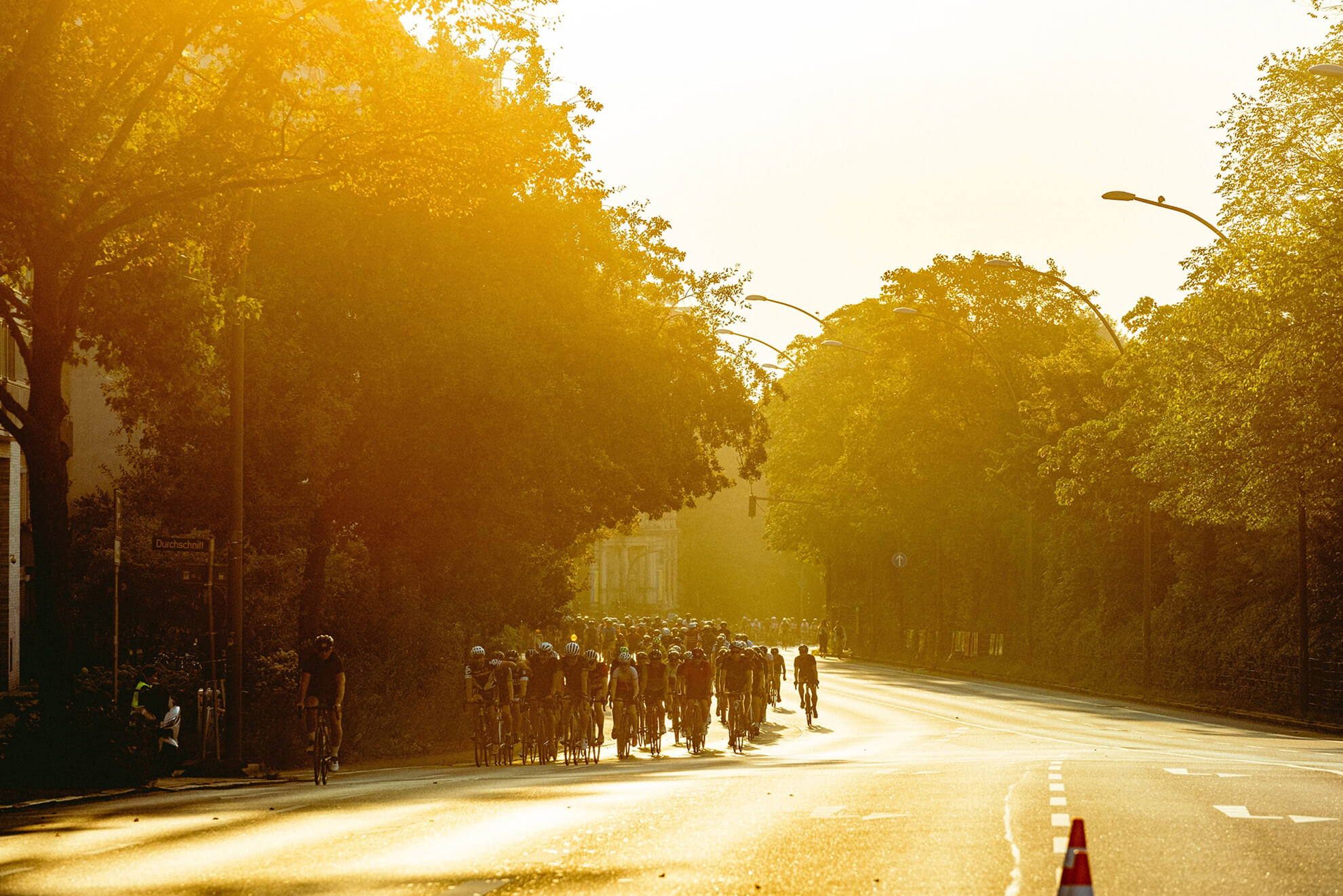 Radfahrer in der Ferne auf einer Straße in der Abenddämmerung, von der Sonne hinterleuchtet.