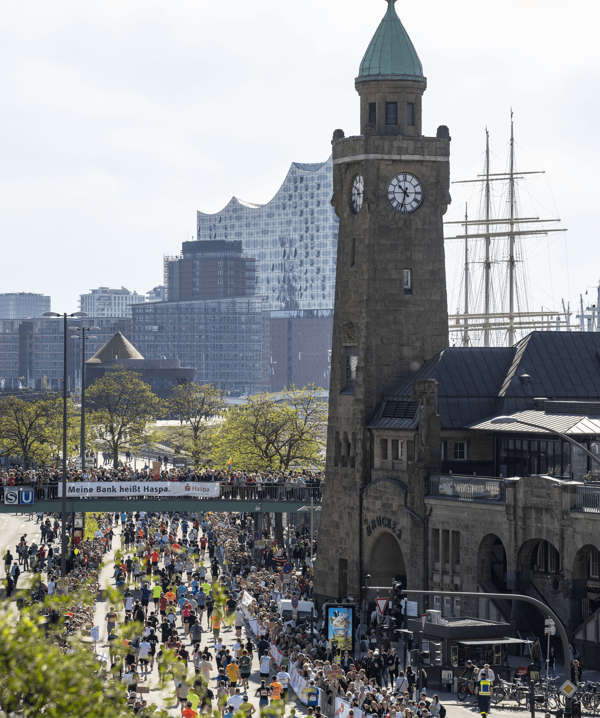 Läufer passieren einen historischen Uhrenturm mit der Elbphilharmonie im Hintergrund.