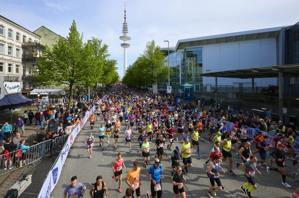 Die Marathon-Läufer rennen auf einer mit Zuschauern gesäumten Straße, ein Fernsehturm ist zu sehen.