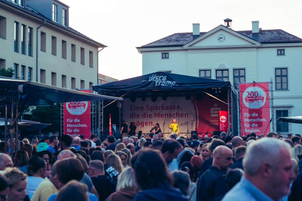 Eine belebte Menschenmenge vor einer Bühne auf einem Platz.